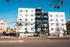 Contemporary apartment building with multiple balconies, set against a clear blue sky, featuring palm trees and a vibrant neighborhood setting.