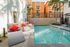 Inviting outdoor swimming pool area with chic lounge chairs and vibrant red cushions, surrounded by modern apartments and lush palm trees.
