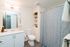 Modern bathroom featuring sleek white cabinetry, stylish patterned shower curtain, and integrated shelving for a clean and organized look.