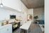 Modern apartment with sleek kitchen featuring white cabinetry, stainless steel appliances, and a cozy living area accented by concrete walls and stylish decor.