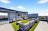 Chic rooftop lounge with stylish seating, green artificial turf, and panoramic city views under a clear blue sky.