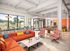 Vibrant communal lounge featuring modern orange sofas, patterned chairs, and large windows with abundant natural light.