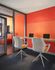 Bright, modern workspace with vibrant orange walls, featuring two sleek desks and chairs, ideal for productive creativity.