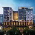 Modern urban apartment complex with illuminated facades, featuring rooftop terraces and panoramic city views at dusk.