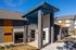 Modern apartment leasing office with stylish stone exterior and vibrant orange accents under a clear blue sky.