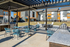 Modern outdoor patio area with stylish seating, barbecue grill, and pergola in front of colorful residential buildings.
