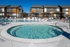 Luxurious apartment complex with a modern outdoor pool and spa area, featuring stylish lounge chairs under vibrant pergolas, perfect for relaxation and leisure.