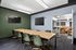 Contemporary conference room featuring elegant green chairs, a wooden table, wall-mounted screens, and a sleek adjoining lounge area with vibrant orange seating.