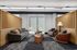 Chic office lounge featuring a sleek grey sofa, stylish armchairs, and a modern coffee table arrangement against a backdrop of elegant wooden partitions.