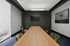 Modern conference room with a sleek wooden table, plush green chairs, and a large wall-mounted TV, perfect for productive meetings.