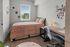 Charming bedroom with a cozy bed, modern desk setup, and vibrant wall art, enhanced by natural light from a large window.