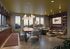 Chic living and dining area with vibrant decor, large windows offering stunning views, and a cozy seating nook with a brick accent wall.