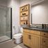 Modern bathroom featuring a sleek glass shower, stylish vanity with granite countertop, and elegant wood shelving for a luxurious touch.
