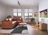 Inviting living room with a sleek leather sofa, stylish decor, large windows, and a flat-screen TV, offering a blend of comfort and modern elegance.