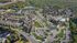 Expansive aerial view of a charming residential community featuring elegant houses, abundant greenery, serene ponds, and inviting amenities, all set amidst a tranquil forest landscape.