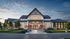 Charming modern farmhouse with large windows, inviting front entrance, and lush landscaped gardens, showcasing an elegant and welcoming ambiance at sunset.