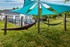 Charming outdoor area featuring colorful hammocks under stylish blue sunshades, perfect for relaxation, with a modern clubhouse in the background.