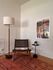 Chic living space with a woven chair, stylish floor lamp, and modern art, complemented by a vibrant patterned rug and a sleek side table with a plant.