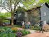 Charming residential home surrounded by lush greenery and bright flowers, with people enjoying a stroll along the scenic brick pathway.