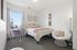 Bright and cozy bedroom with a stylishly decorated bed, modern workspace, and a comfy papasan chair, all illuminated by natural light from a large window.