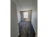 Carpeted room with gray walls and a square window on the wall opposite of the door bringing in natural light.