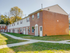 Row of townhouses at Catons Villas South with red brick and white siding, sidewalks, green grass, and nearby trees.