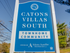Blue sign for Catons Villas South Townhome Community by Adams-Aumiller Properties, with trees and power lines in background.