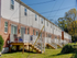 Row of brick townhouses at Catons Villas South with white siding, wooden decks, staircases to grassy yards, and clear sky with power lines.