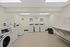 Bright, clean laundry room at Catons Villas South with four dryers, two washers, wall clock, art, and folding table.