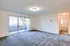 A spacious empty living room in Allyson Gardens Apartments II, featuring a carpet and a sliding glass door.
