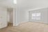 Open concept sunlit empty living room with large window and beige carpet flooring.