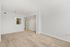 Bright living area with plush beige carpet, white walls, and modern light fixture leading to kitchen area.