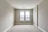 A sunlit room with two large windows and plush carpeting, providing a perfect blank canvas for personalization.