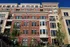 A picturesque apartment building with a red brick exterior, bay windows, and vibrant greenery.