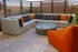 A stylish outdoor patio with a cozy L-shaped sofa, vibrant orange cushions, and a sleek circular table.
