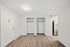 Spacious room with open double closets and sleek hardwood flooring, adjacent to a modern kitchen.