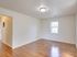 A sunlit empty room with polished hardwood floors and a large window, offering plenty of natural light.