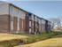 A modern apartment building with a facade, located in a scenic suburban area and surrounded by well-maintained green spaces.