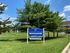 A lush green lawn featuring a blue sign for Caton Villas Apartments, under a clear blue skies.