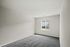 A roomy, empty bedroom featuring soft gray carpet flooring and a large window that lets in plenty of natural light.