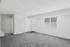 A spacious living room with large windows, plush gray carpeting, and plenty of natural light.