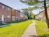 A peaceful townhouse community featuring well-maintained green lawns, charming brick buildings, and a walkway in the middle of the complex.