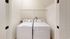 Elegant laundry room with a modern washer and dryer set, featuring sleek white design and ample shelving space at Emerson Flats.