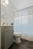 Bright and modern bathroom with sleek gray vanity, elegant fixtures, and soft blue shower curtain.