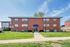 Inviting red brick apartment building with charming windows, surrounded by lush green lawn under a serene blue sky.