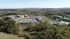 Serene aerial view of a modern apartment complex nestled in a lush, scenic landscape with nearby wooded areas and expansive green fields.
