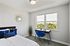 Bright and serene bedroom with modern decor, featuring a stylish desk and chair by a large window overlooking lush greenery.