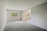 Bright and spacious room with gray carpeting, featuring large windows for abundant natural light and serene views of greenery.