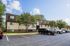 Charming apartment building with a modern exterior, surrounded by lush trees and ample parking space under a clear blue sky.