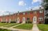 Charming brick townhouse with lush green lawns and vibrant flower gardens under a bright blue sky.